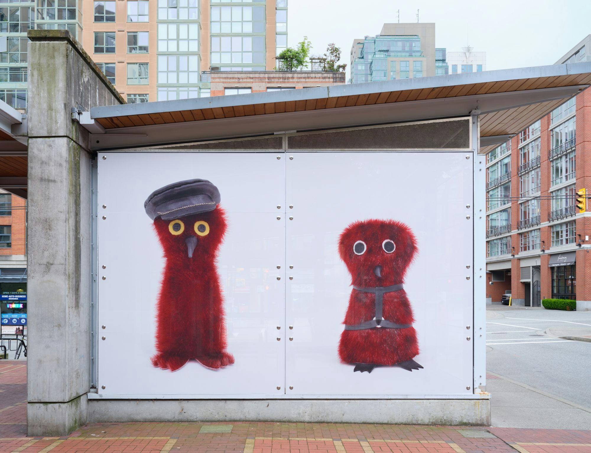 A frontal view of a SkyTrain station with photographs depicting Ookpik figures, or stuffed owl toys, in its windows. The Ookpiit both have red fur and sport leather accessories.