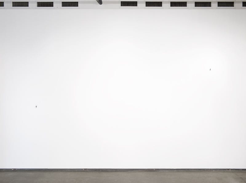 Two mosquito sculptures by Xu Zhen are barely visible in this image. Installed on a white gallery wall, one is on the upper right and the other on the lower left, each dwarfed by the size of the wall.