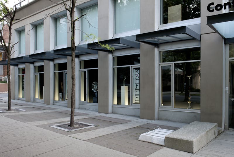 Josephine Meckseper’s sculptures installed in CAG’s facade windows, a mannequin hand, a car wheel, and others. Many of these sculptures have metallic, reflective surfaces and are displayed on plinths.