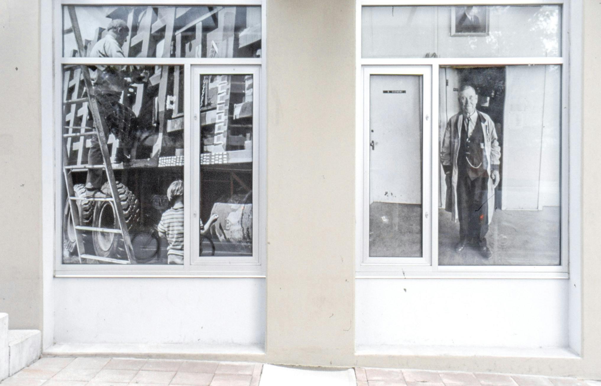 Two of CAG’s window spaces are visible in this photograph. Enlarged images from different black and white photographs cover those windows. Both images depict people but in different social settings.