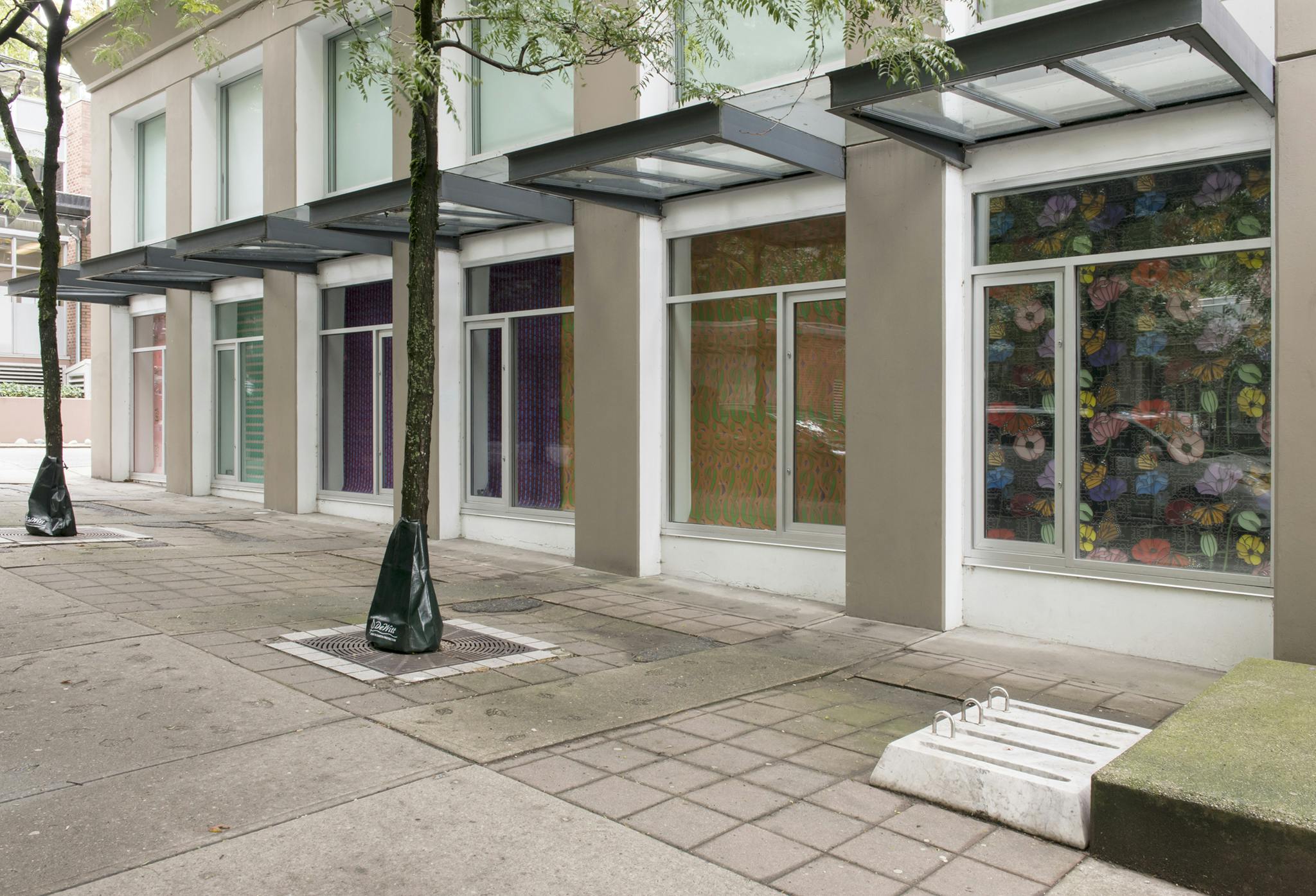 Exterior of the Contemporary Art Gallery displaying the work of Julian Yi-Zhong Hou. Boldly patterned paper prints hang from the street level windows. Colours of pink, green, purple and yellow are prominent.