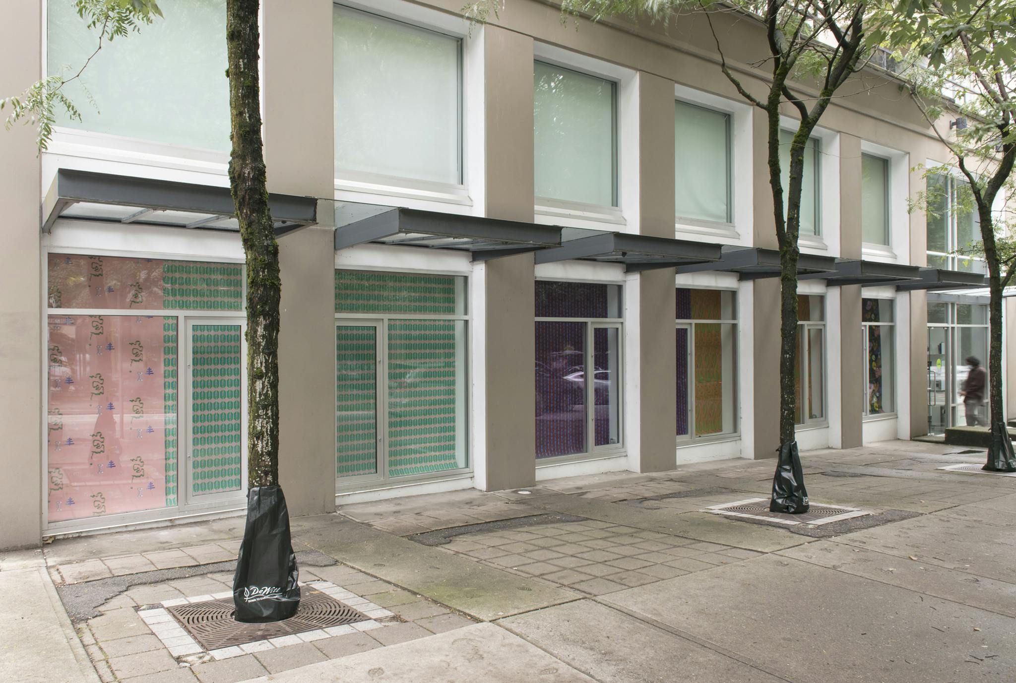 Exterior of the Contemporary Art Gallery displaying the work of Julian Yi-Zhong Hou. Uniquely patterned paper hangs from the street level windows. Colours of pink, green, purple and yellow are prominent.