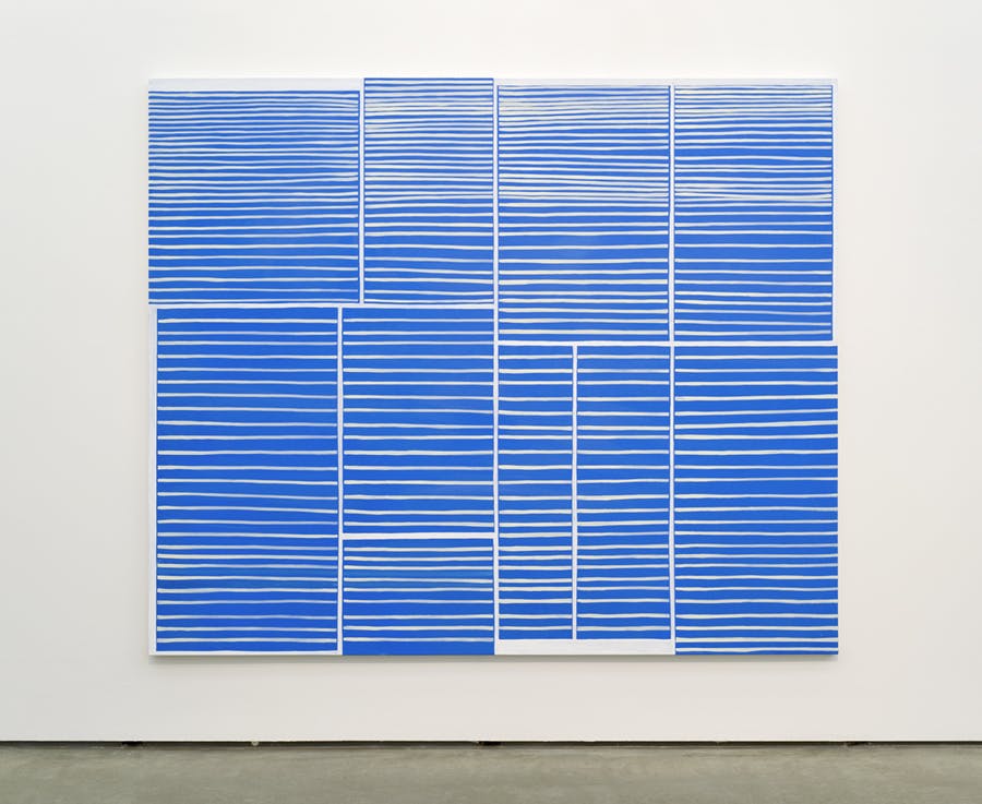 A large scale painting hangs on a gallery wall. The painting is made up of blue lines on a white background. The lines are laid out in such a way that they form a series of rectangles. 