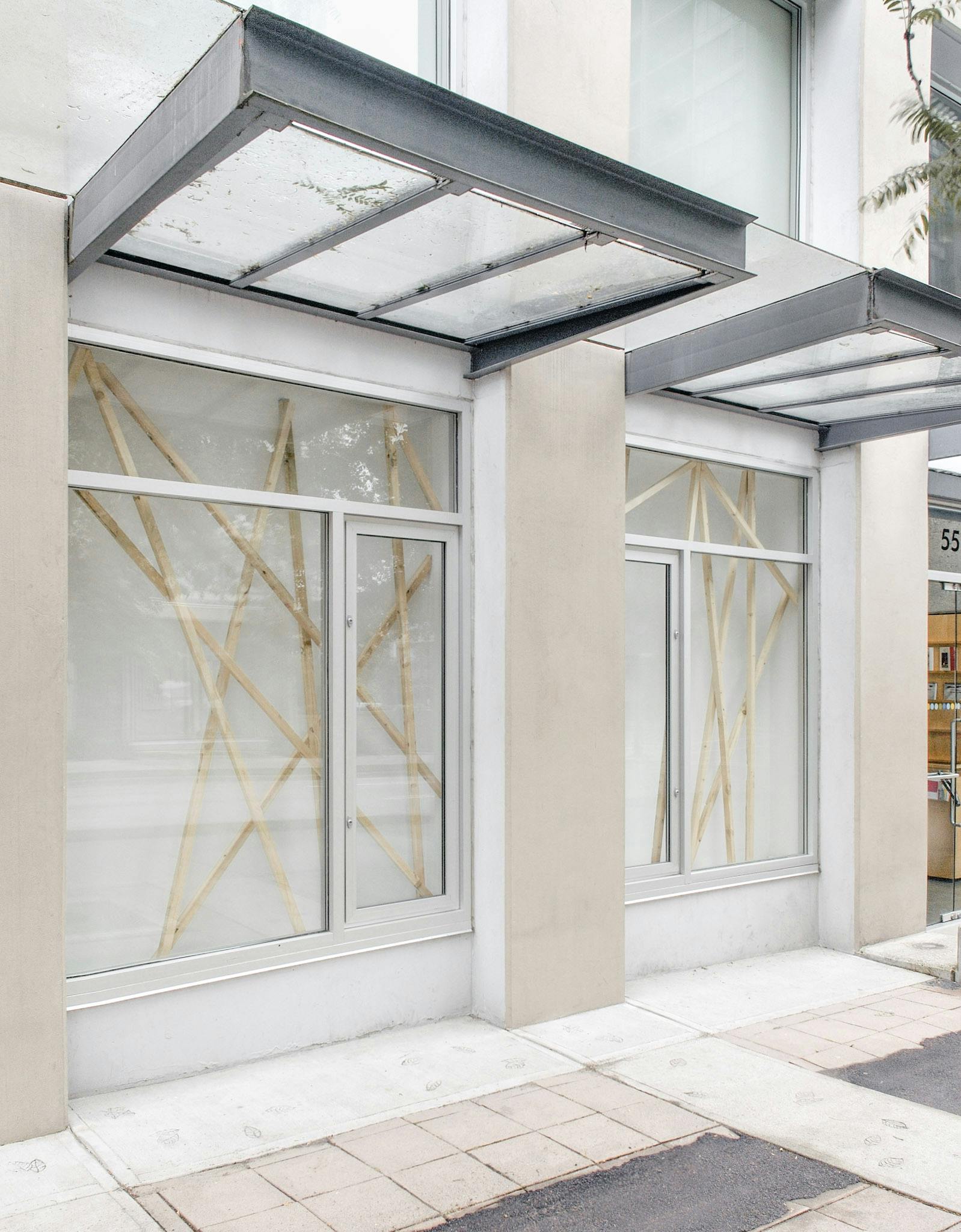 This image shows two of CAG’s window spaces, in which Elspeth Pratt’s installation art is displayed. About ten wooden bars are diagonally placed in each window. No bars parallel to the others. 