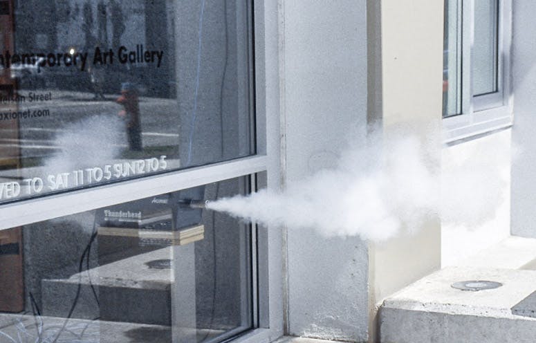 White smoke is coming out of a thin pipe connected to the glass entrance of CAG’s building. The smoke is emitted outside from a black machine placed inside the entrance.