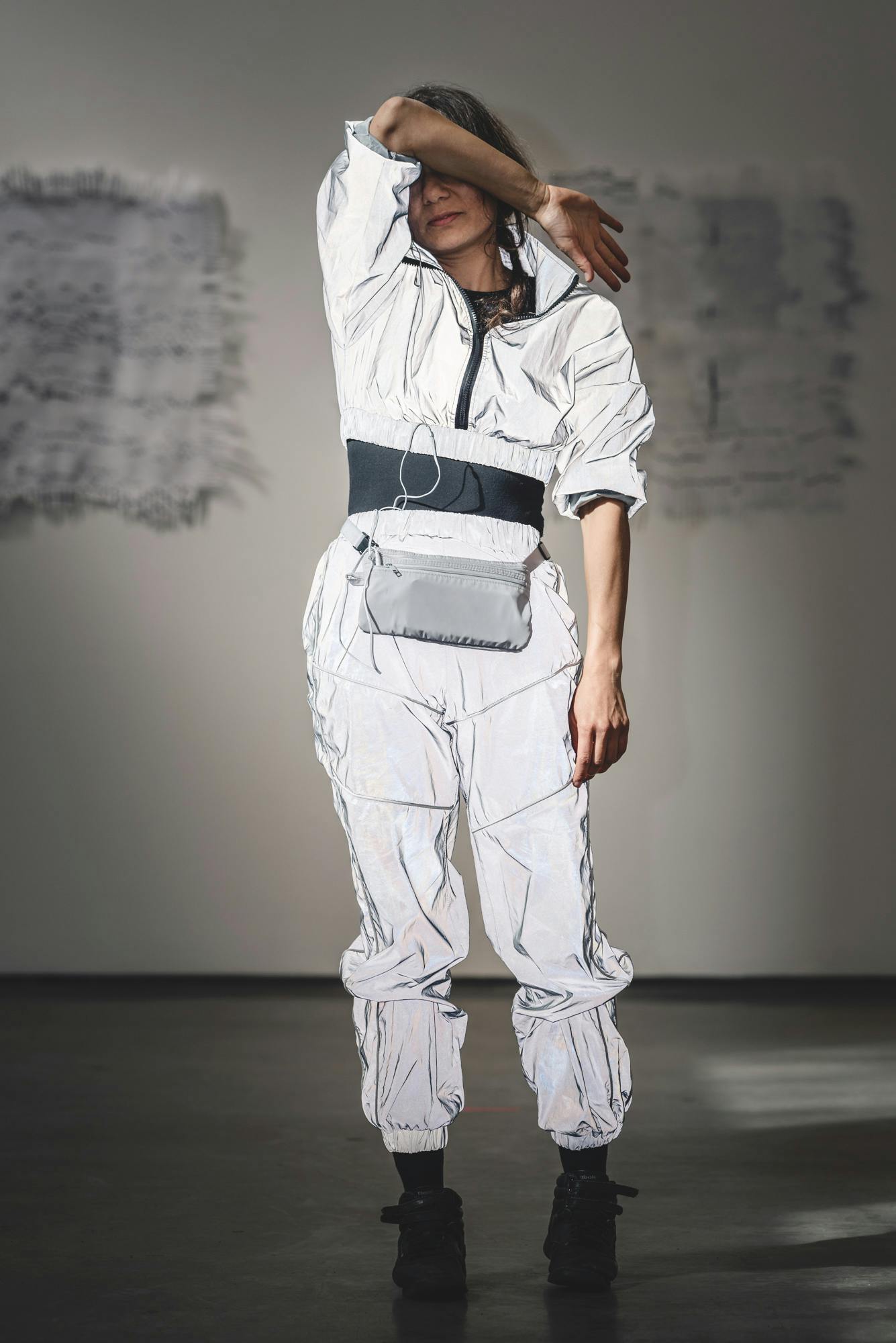 An image of Justine A. Chambers performing choreography in a gallery space. Chambers is wearing a silver jumpsuit. 