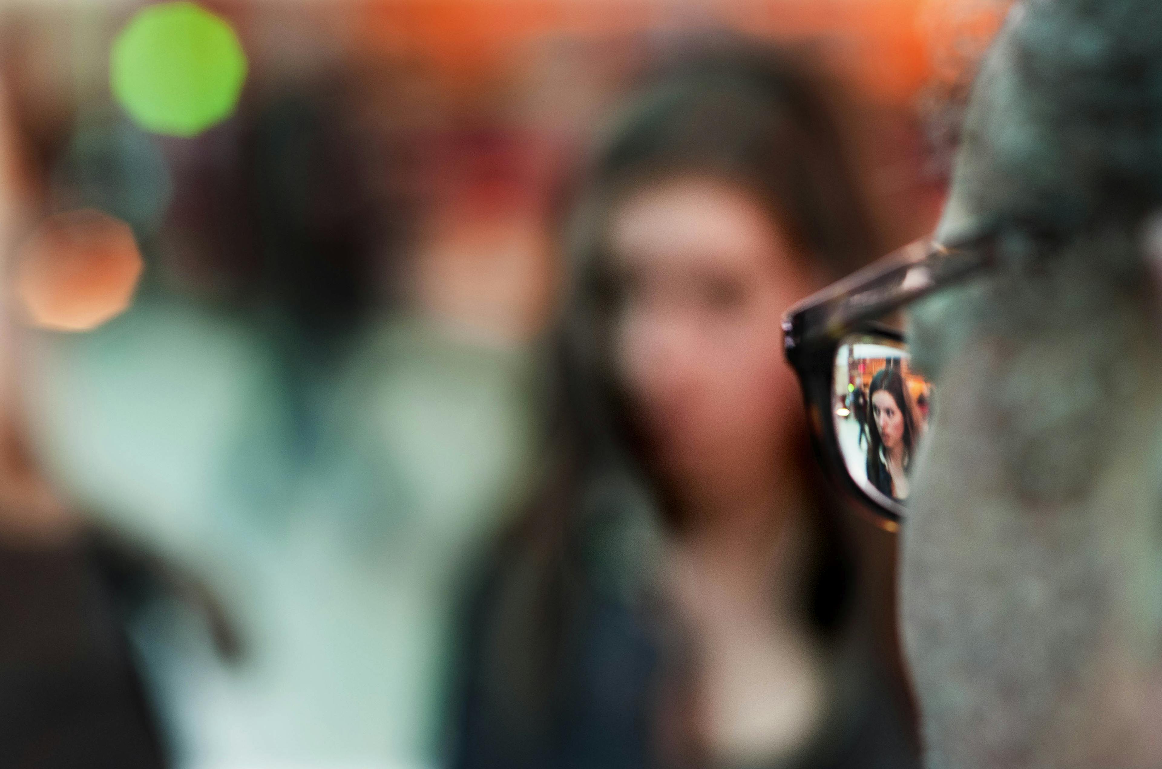 An blurry image focused on the reflection on the glasses worn by a person. 