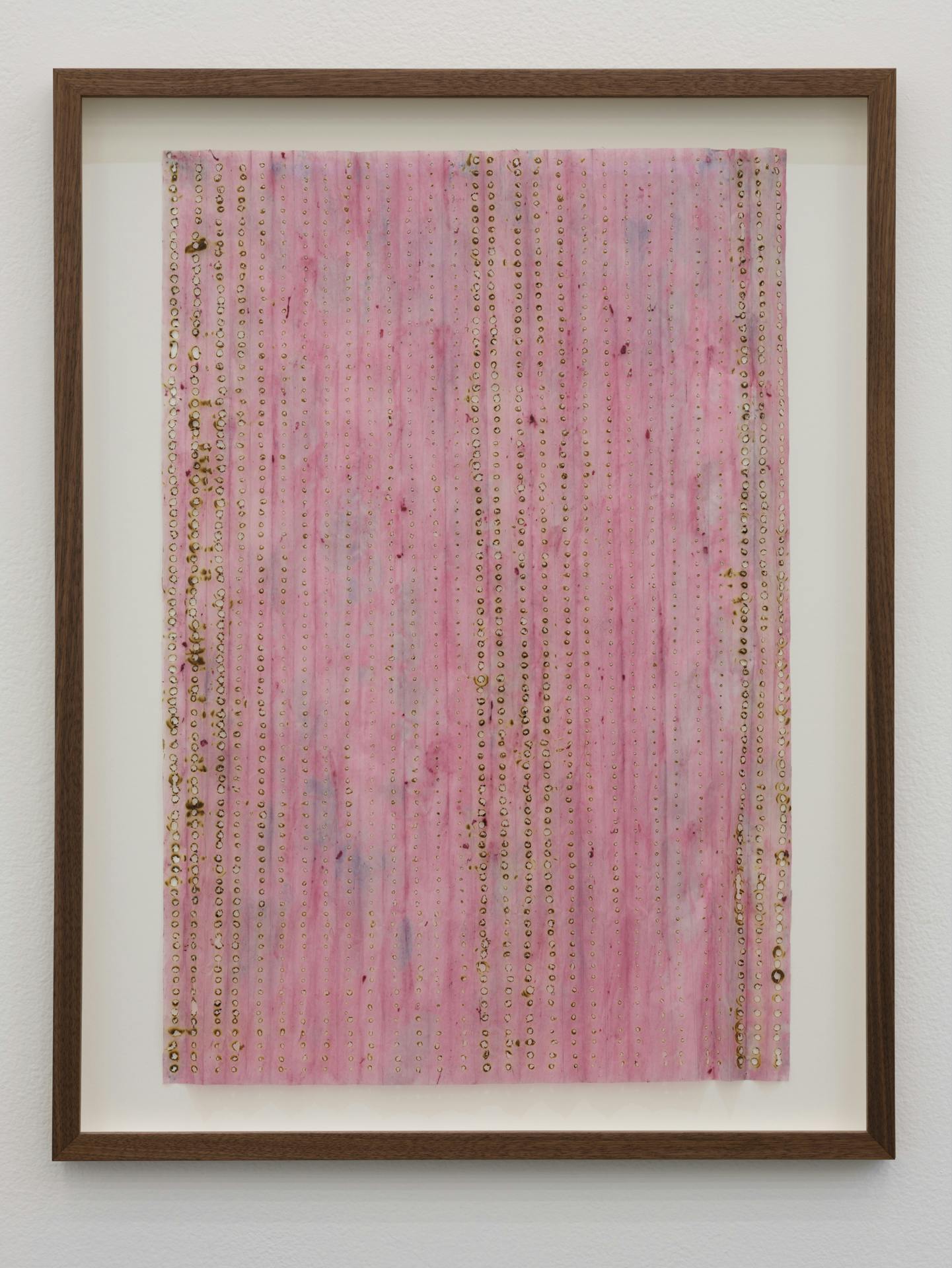 A framed collage with a pink background with small burn holes running up and down collage in columns.