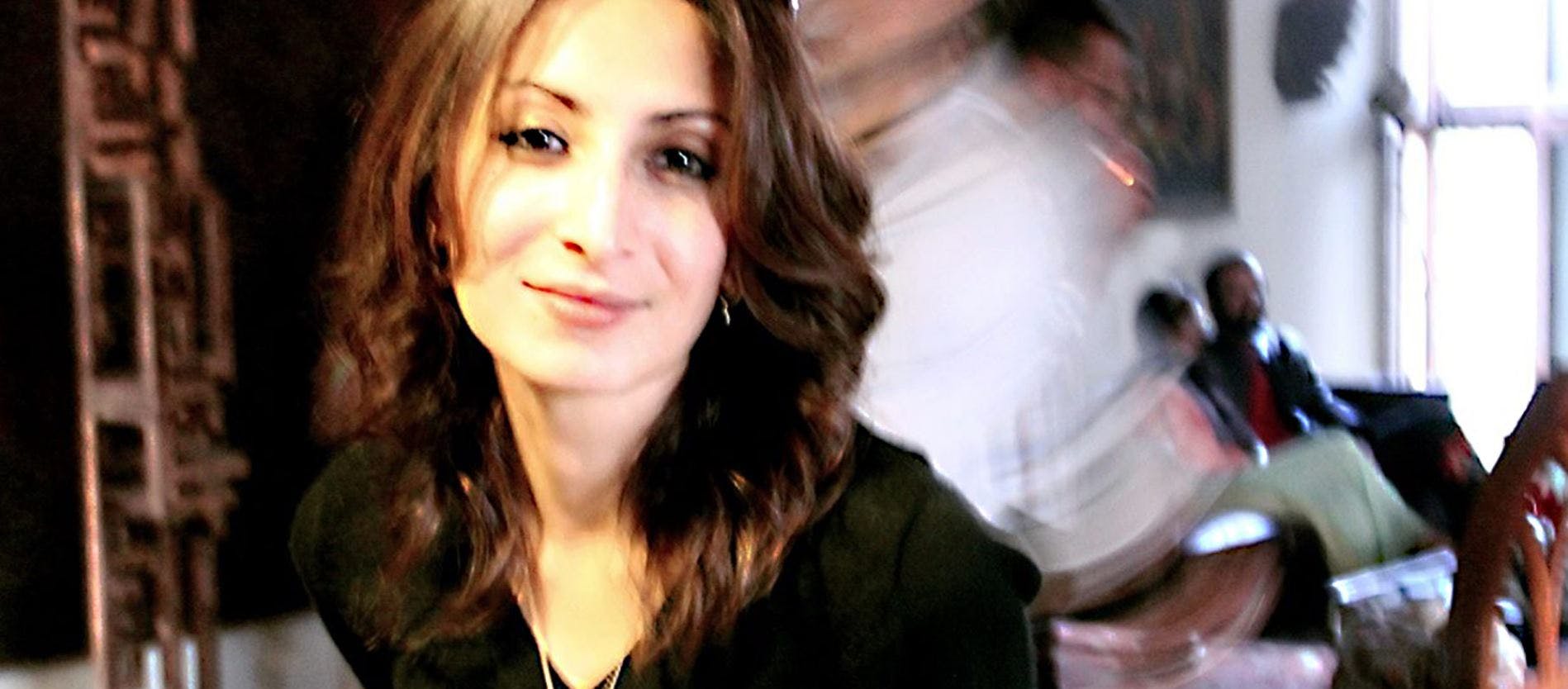 A portrait photograph of Zarmeene Shah. She has a long brown hair and is wearing a black shirt. She smiles directly at the camera. 