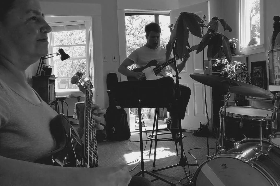 A black and white photograph of Charlene Vickers and Chad MacQuarrie playing guitars inside a house. 
